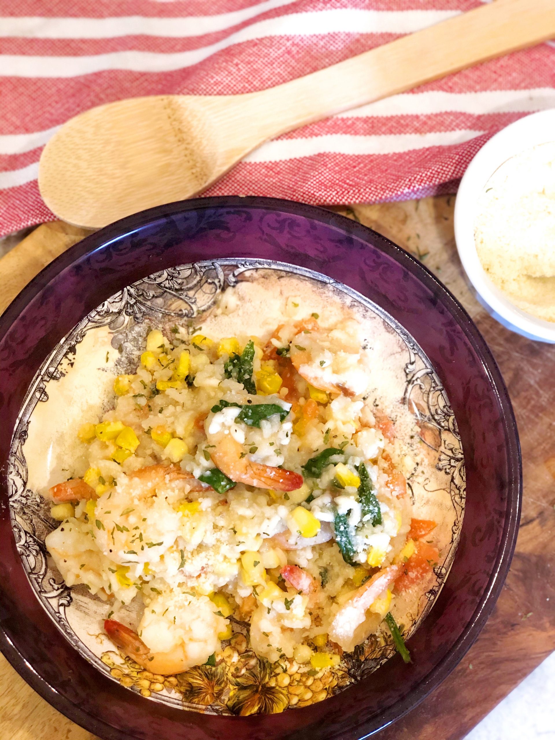 Sweet corn risotto with sauteed shrimp on a wooden board with a wooden spoon and a checkered cloth