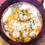 sweet corn risotto with sauteed shrimp in a maroon bowl on a wooden board
