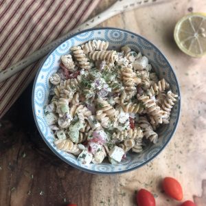 creamy cucumber tomato and chickpea pasta salad in a blue bowl on a wooden board