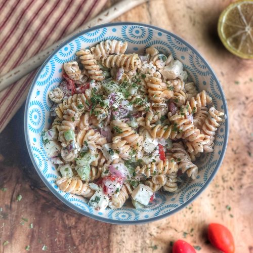 creamy cucumber tomato and chickpea pasta salad in a blue bowl on a wooden board