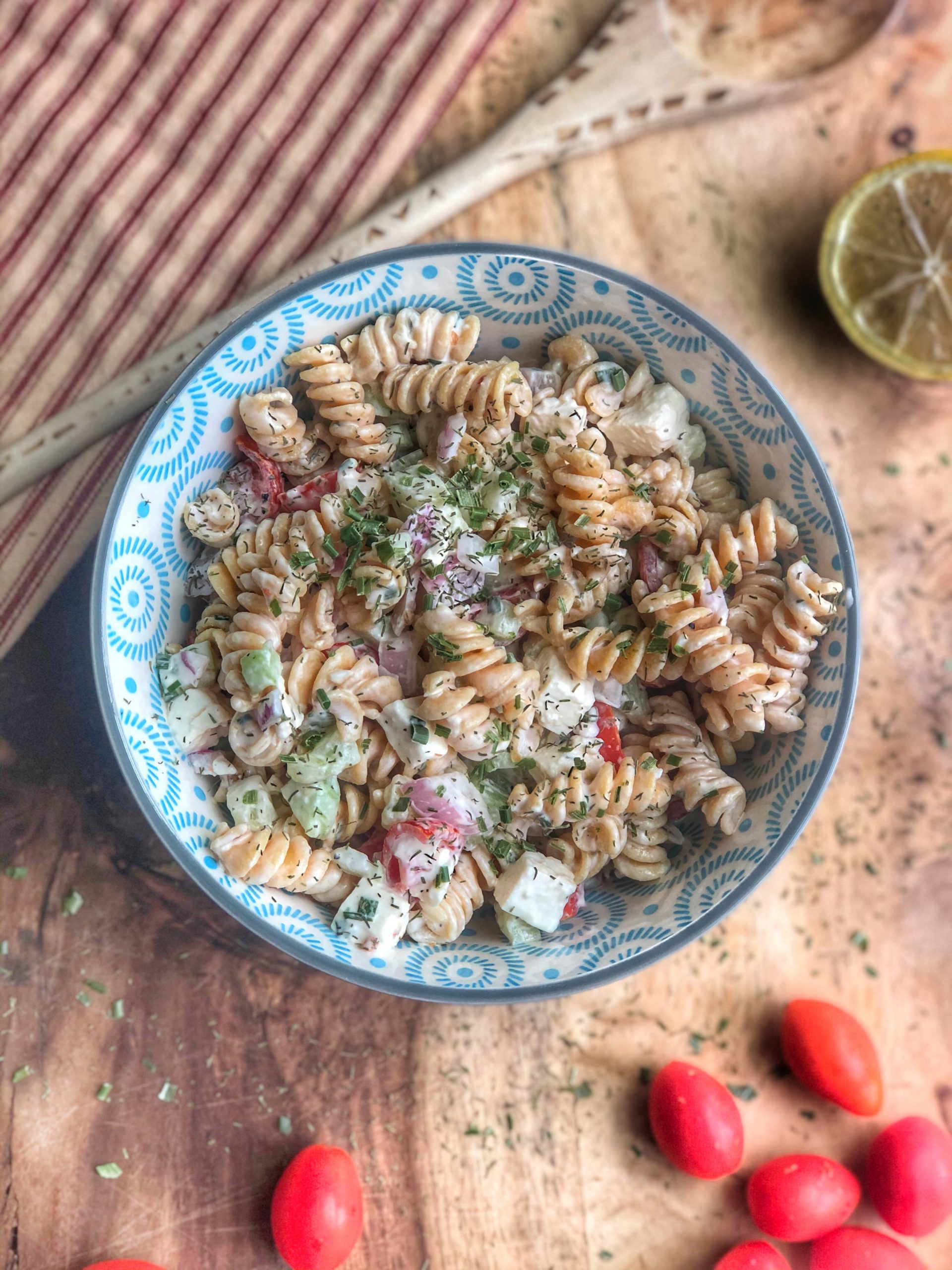 creamy cucumber tomato and chickpea pasta salad in a blue bowl on a wooden board