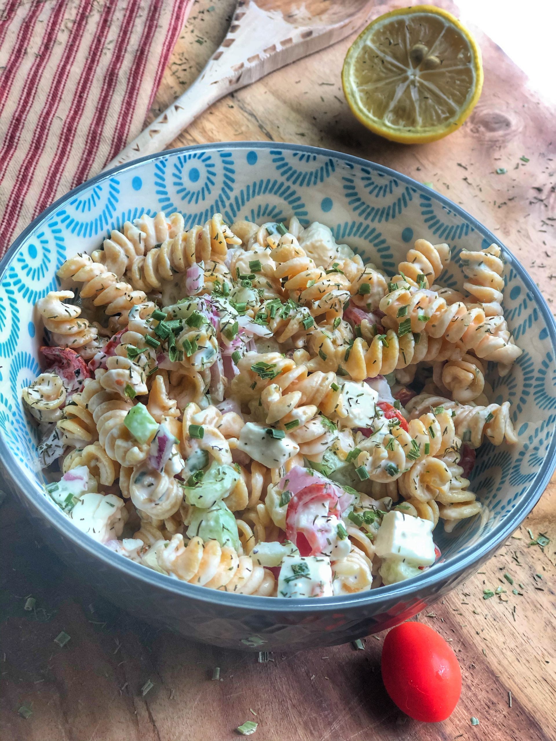 close up of creamy cucumber tomato and chickpea pasta salad in a blue bowl on a wooden board