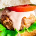 A close up of a turkey burger on a whole wheat bun with tomato, lettuce, and burger sauce.