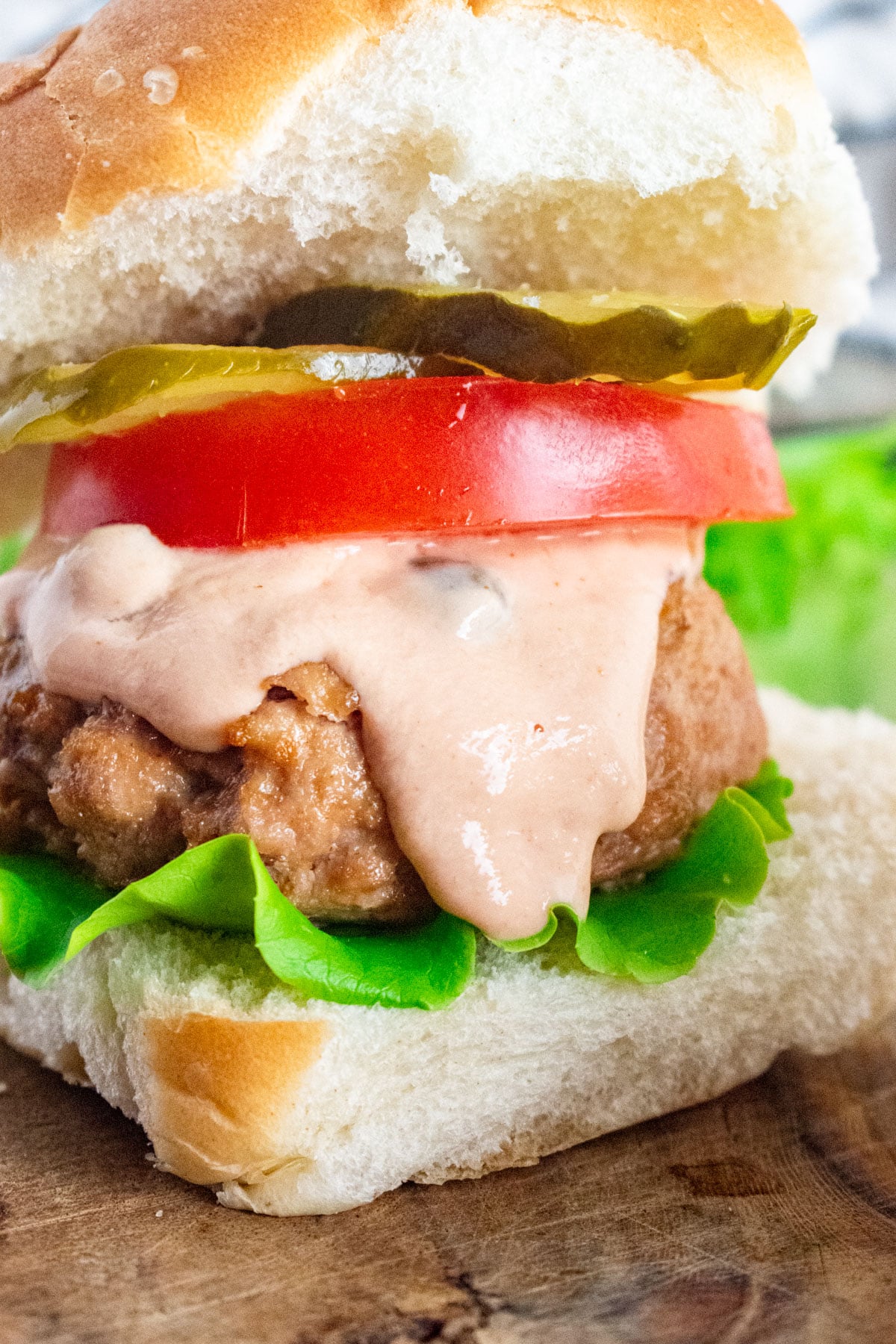 A close up of a turkey burger on a whole wheat bun with lettuce, tomato, pickle, and burger sauce dripping down.