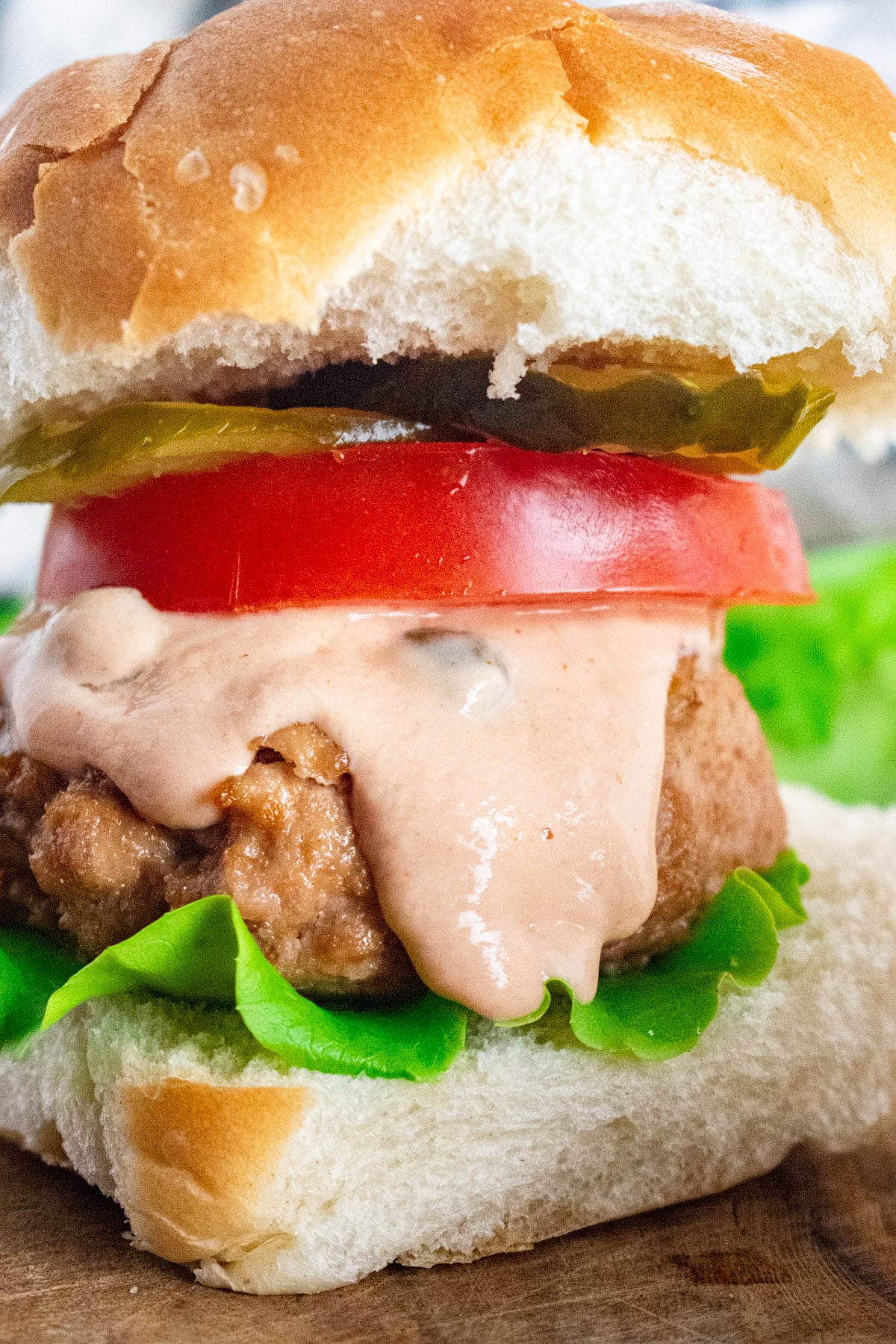 A close up of a turkey burger on a whole wheat bun with lettuce, tomato, pickle, and burger sauce dripping down.
