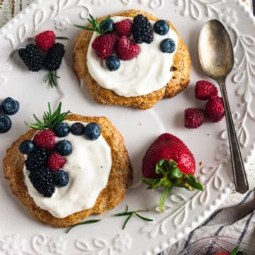Almond cookie fruit tarts on a white plate with fresh scattered fruit about and homemade whipped cream on top.
