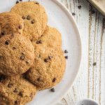 almond flour chocolate chip cookies without butter on a white plate with chocolate chips scattered around