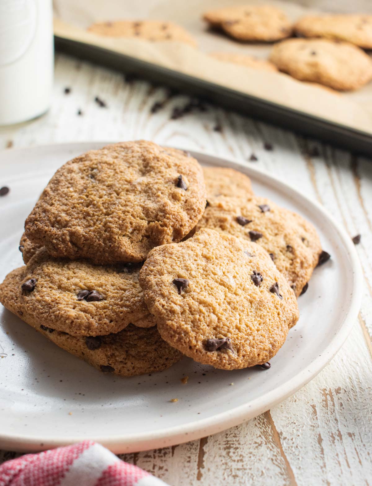 close up of the almond flour chocolate chip cookies without butter on a white plate with chocolate chips scattered around