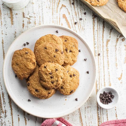 almond flour chocolate chip cookies without butter on a white plate sitting on a white board with a red and white stripped cloth napkin