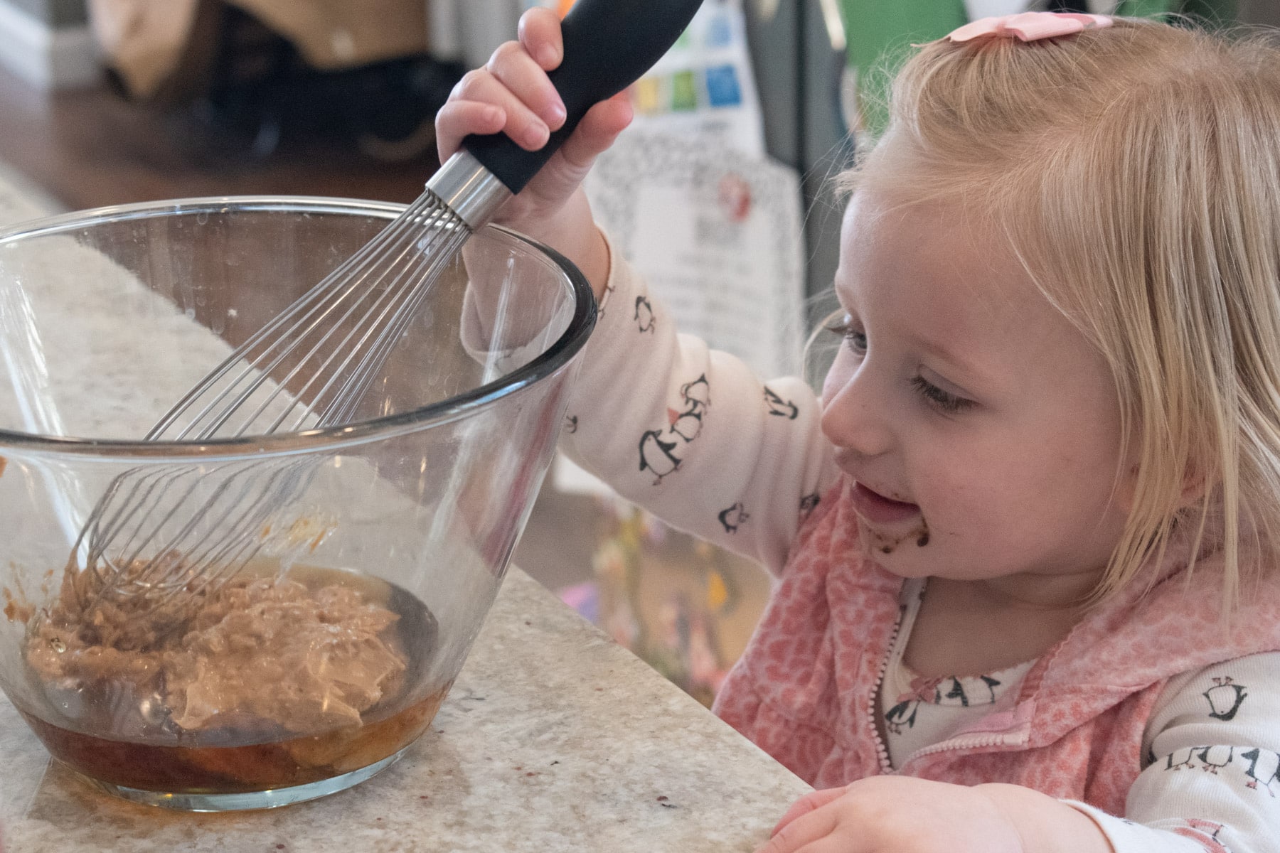 Little blonde girl stirring peanut butter and maple syrup together.