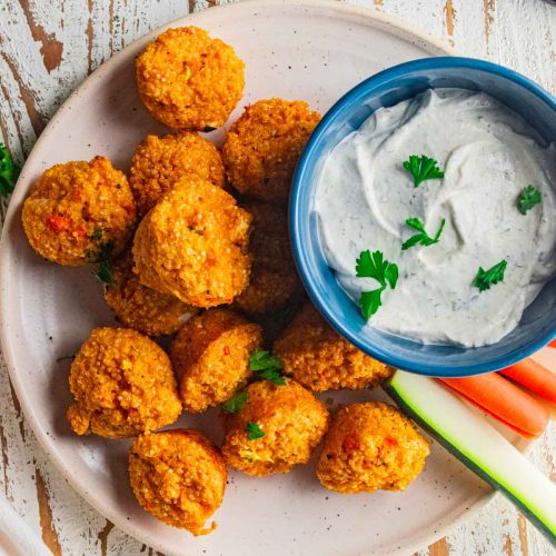 A birds eye view of buffalo quinoa bites and homemade ranch dip on cream colored plate with slices of carrots and celery.