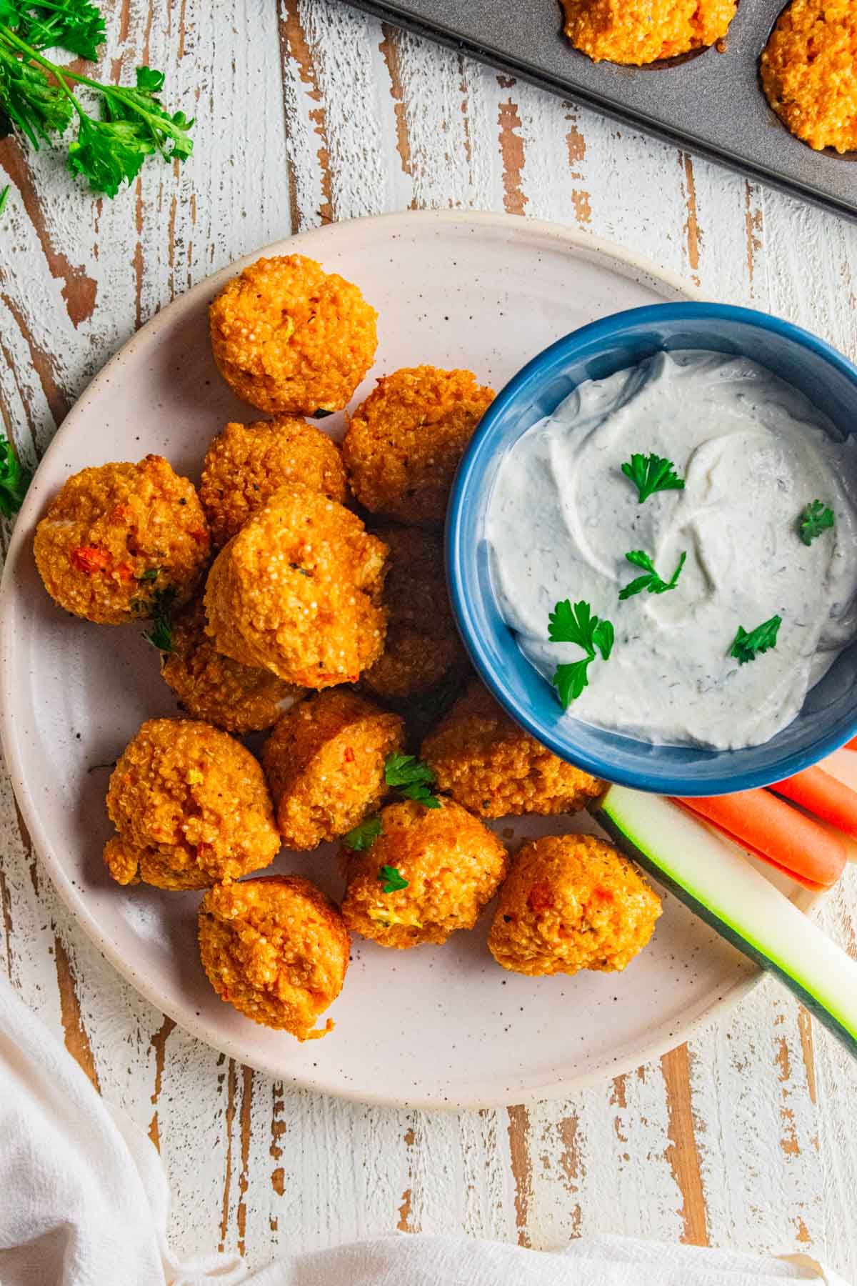 A birds eye view of buffalo quinoa bites and homemade ranch dip on cream colored plate with slices of carrots and celery.