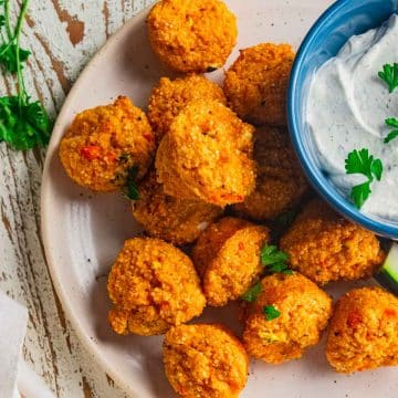 A birds eye view of buffalo quinoa bites on a cream colored plate with slices of carrots and celery and a bowl of homemade ranch dip in a blue bowl.