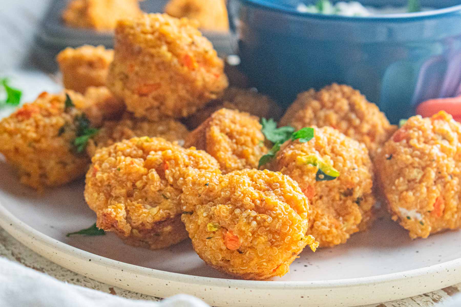 A close up of buffalo quinoa balls on a cream colored plate with a blue bowl on plate next to the balls.