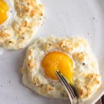 Cloud eggs on white plate with a fork breaking the yolk.