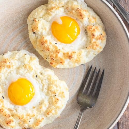 A birds-eye view of cloud eggs on a cream colored dish with a fork laid to the side.