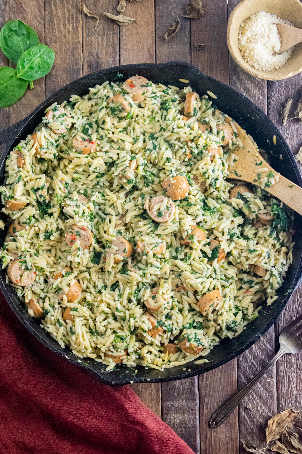 Creamy chicken sausage orzo in a cast iron skillet on a wooden table with a maroon table laid to the side.