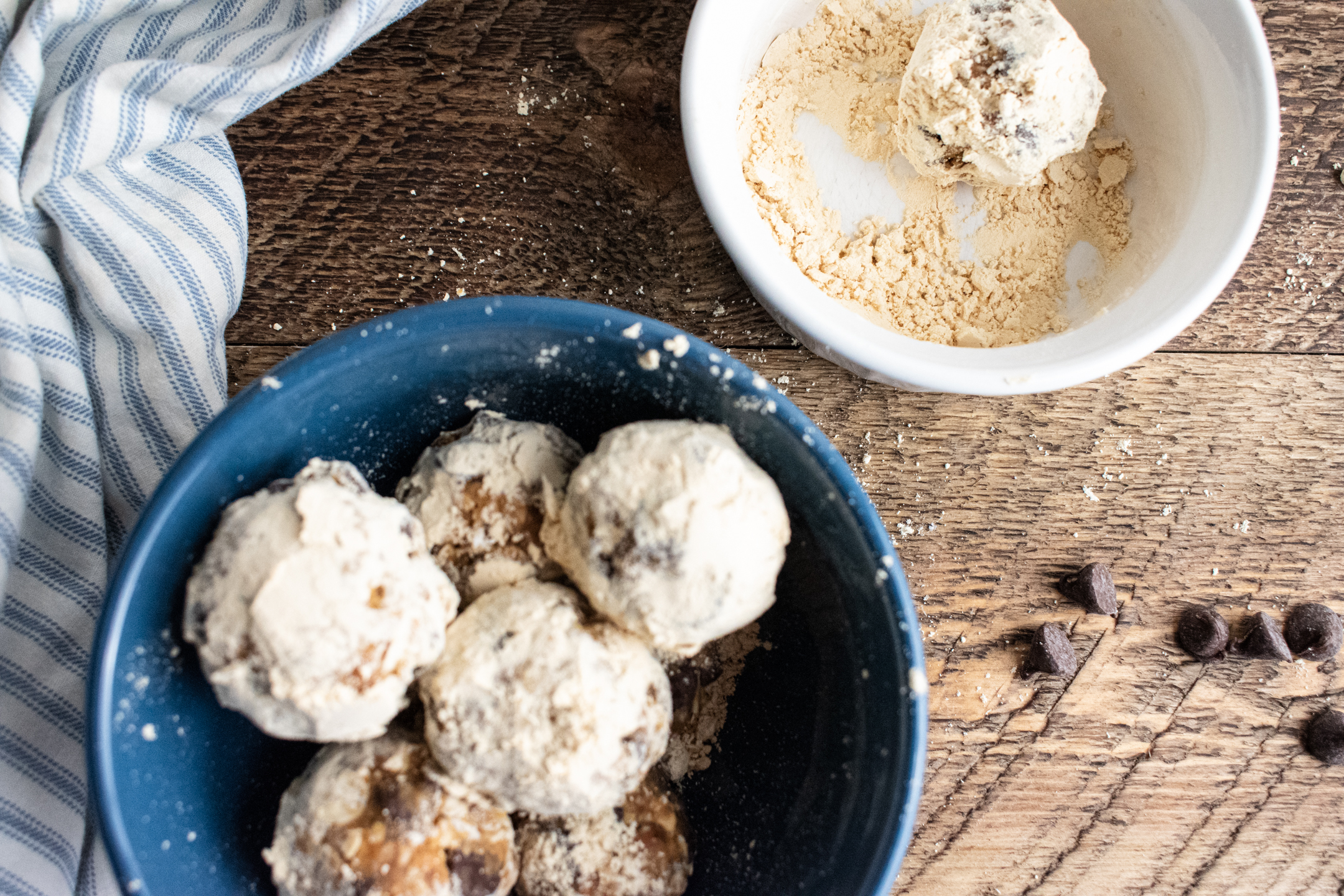 birds eye view of no bake energy bites in a blue bowl and a small white bowl with peanut butter powder in it