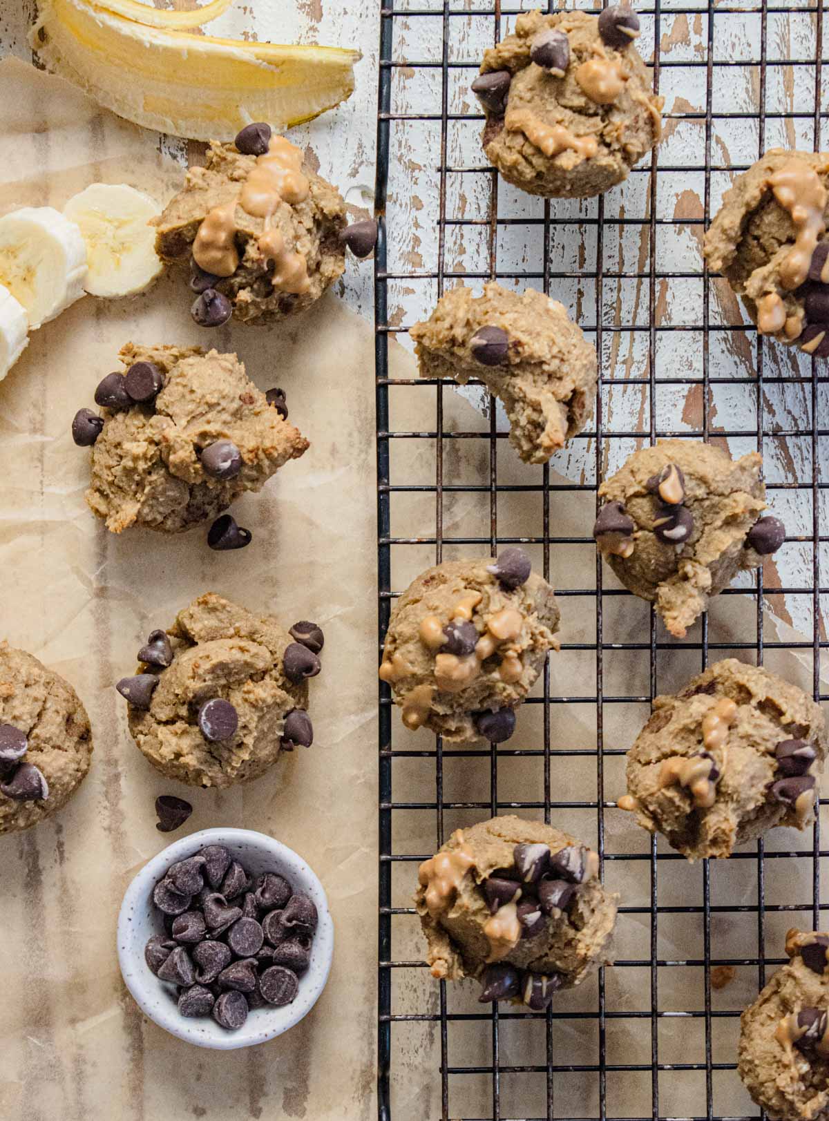 flourless banana muffins on a cooling rack and sitting on parchment paper with a cup of chocolate chips