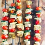 Grilled chicken pesto kabobs on skewers with cherry tomatoes and sliced zucchini and dish of pesto on the side.