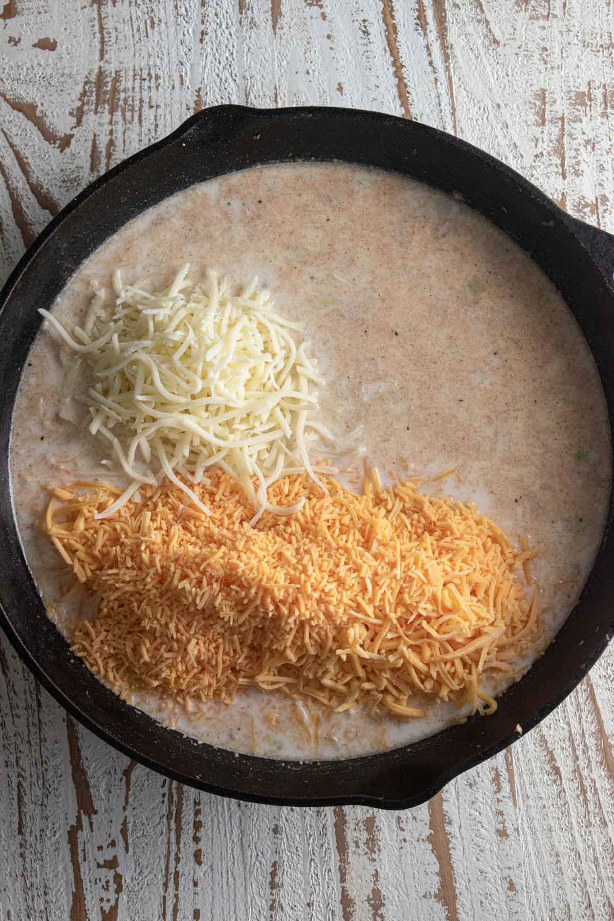 Step 6 - cheeses being added to the mac and cheese in a Lodge cast-iron skillet.