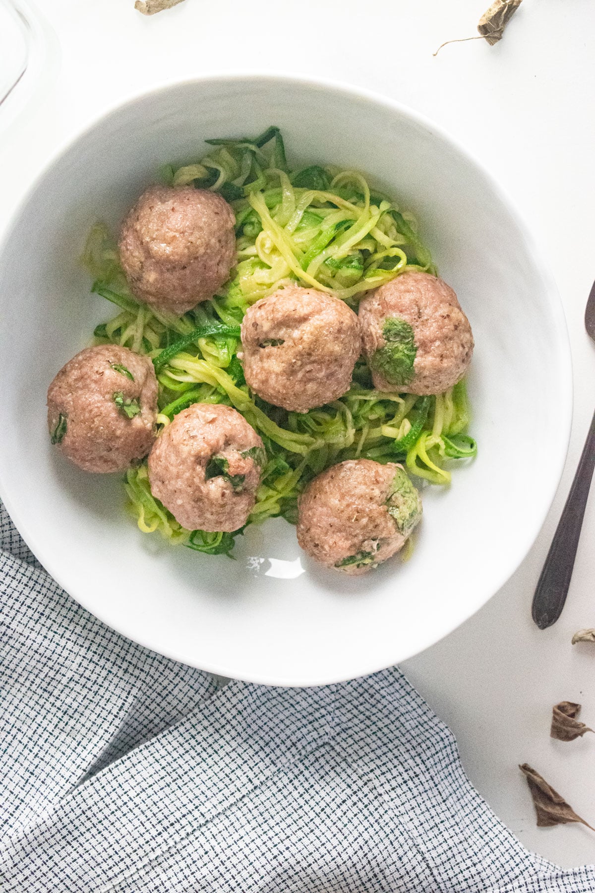 A close up of ground turkey meatballs over zoodles in a white bowl on a white table.