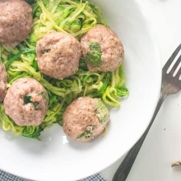 A birds-eye view of ground turkey meatballs in a white dish with a fork plated next to the bowl.