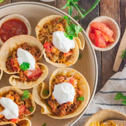 A close up of ground turkey taco cupcakes in a cream colored dish with plain greek yogurt and cilantro on top.