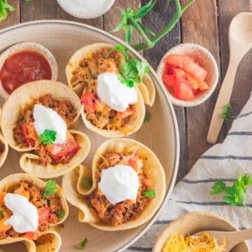 Ground turkey tacos in a cream colored dish on a wooden table with cilantro scattered around.