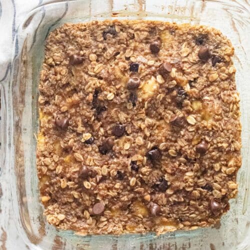 A birds-eye view of oatmeal breakfast bars in a glass dish on a white wooden table.