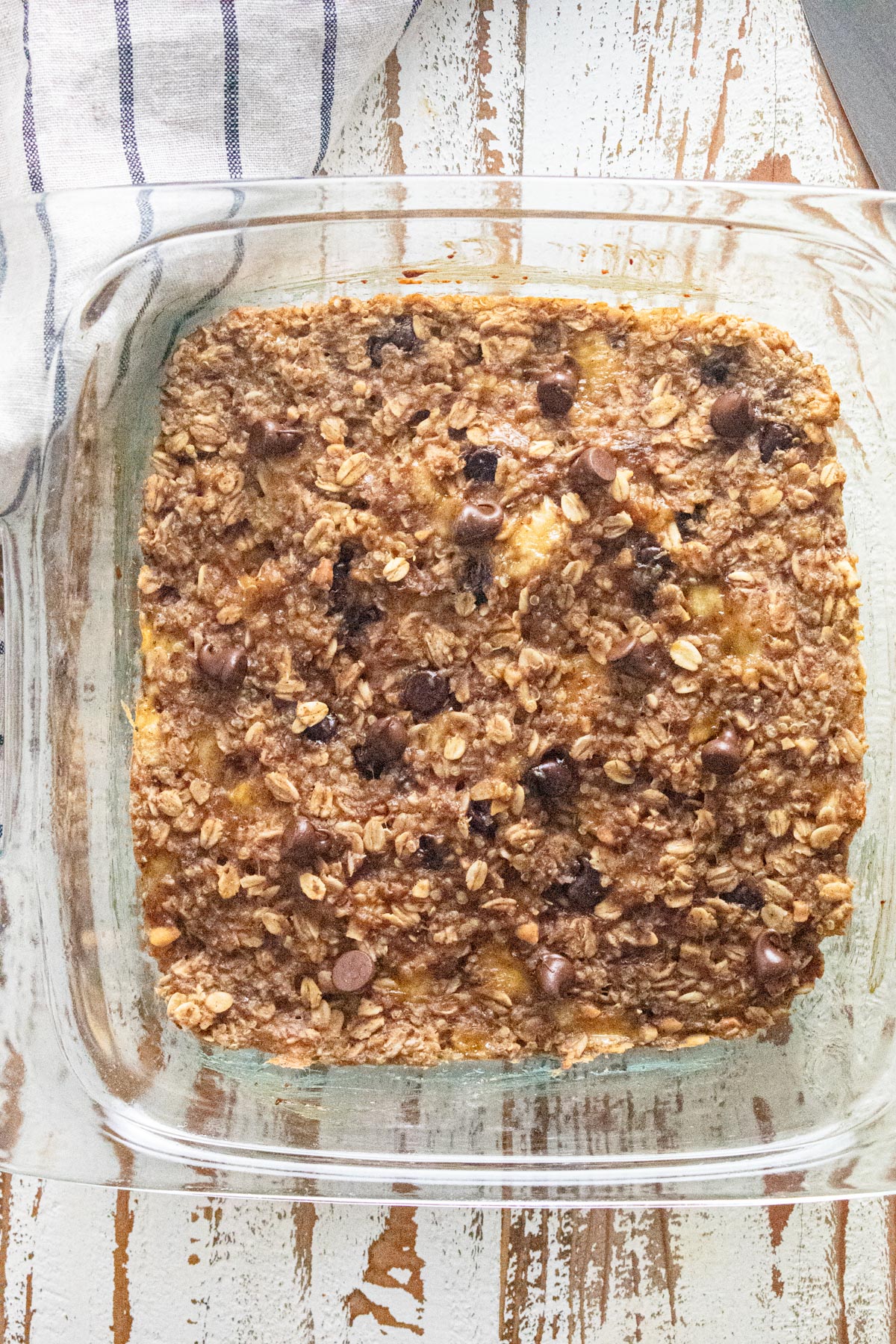 A birds-eye view of oatmeal breakfast bars in a glass dish on a white wooden table.