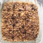 A birds-eye view of oatmeal breakfast bars in a glass dish on a white wooden table.