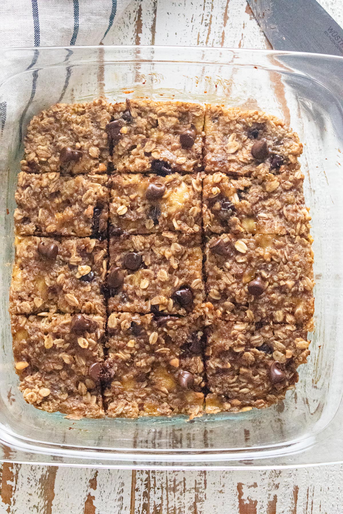 A birds-eye view of oatmeal breakfast bars in a glass dish on a white wooden table.