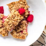 Berry oatmeal breakfast bars in a white bowl with raspberries scattered on top.