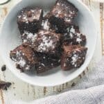 Chocolate chickpea brownies in a white bowl topped with white powdered sugar and a glass of milk on the side.
