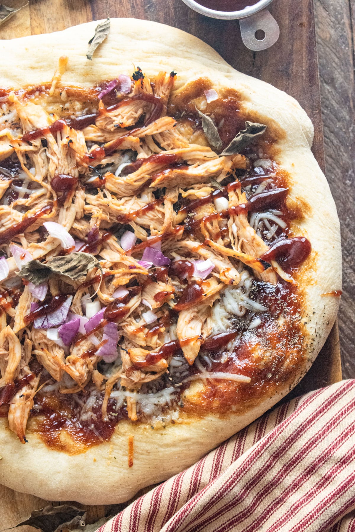 BBQ chicken pizza on a wooden cutting board with a striped napkin laid to the side.