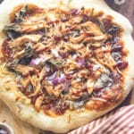 BBQ chicken pizza on a wooden cutting board with a striped napkin laid to the side.