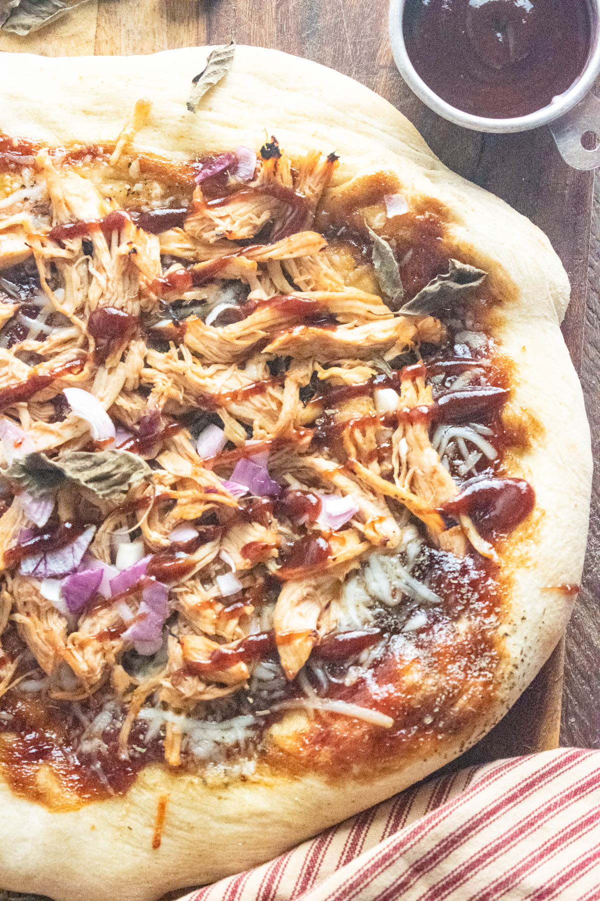 BBQ chicken pizza on a wooden cutting board with a dish of BBQ sauce to the side.
