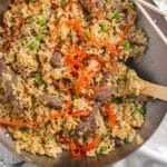 Beef fried rice in a wok with a wooden spoon slotted in the side.