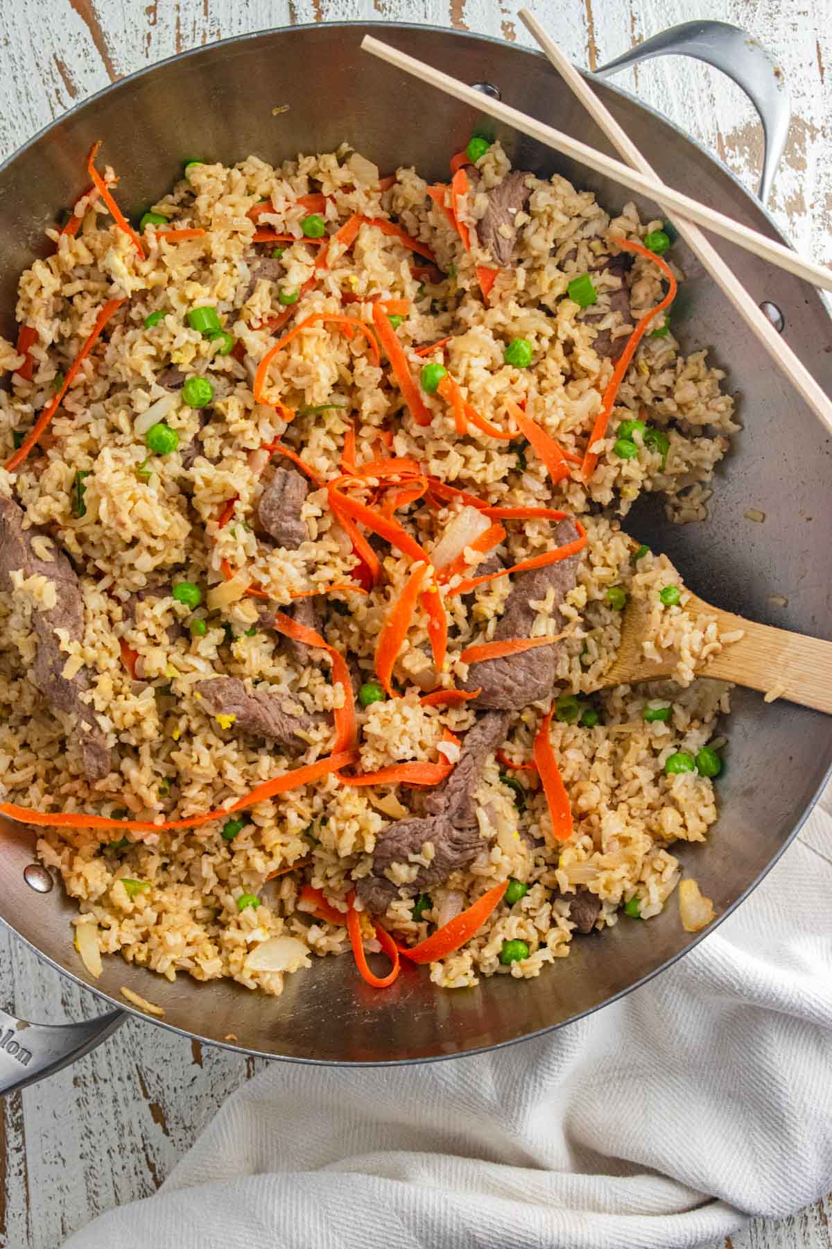 Beef fried rice in a wok with a wooden spoon slotted in the side.