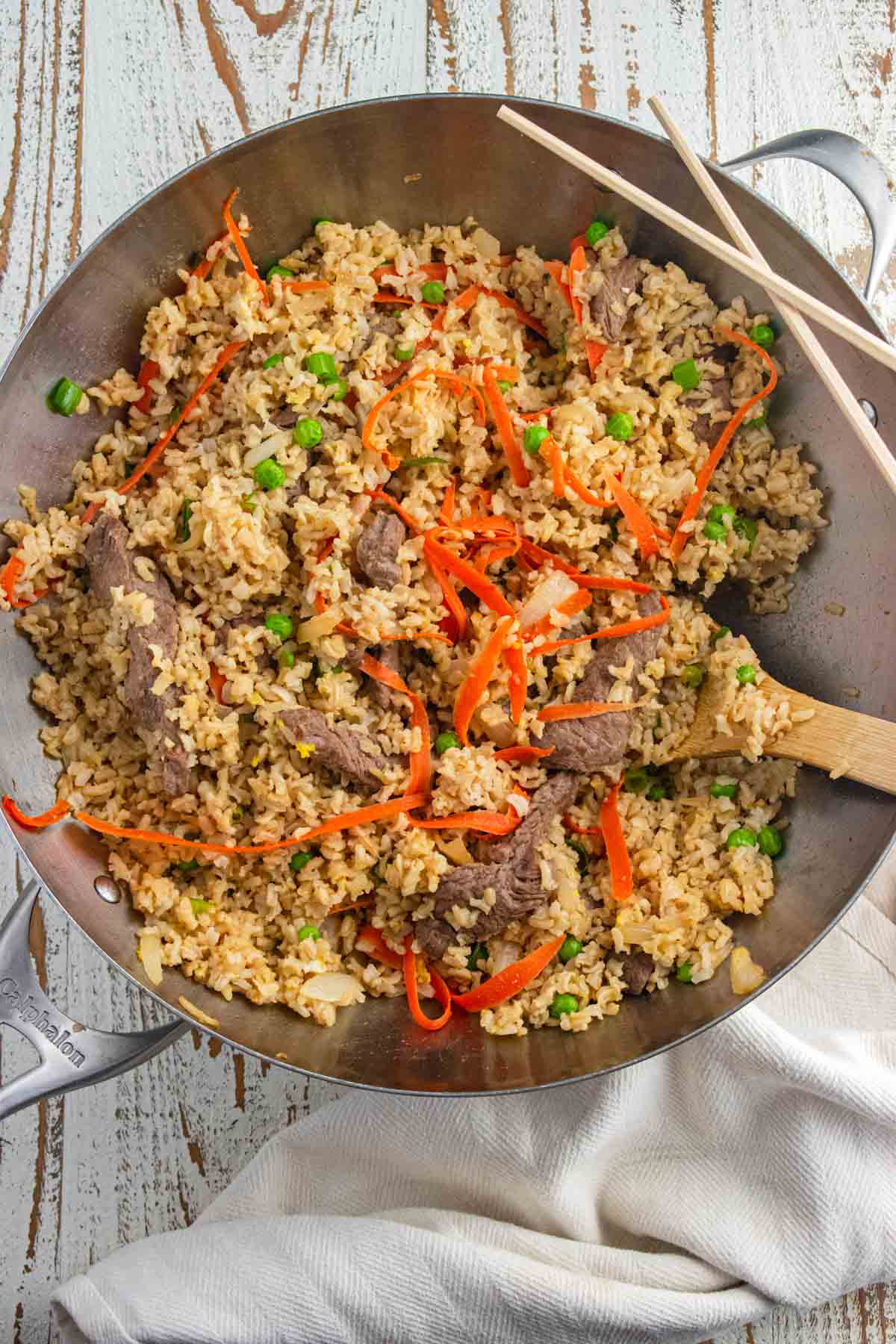 Close up of easy beef fried rice in a wok with a slotted wooden spoon and two chop sticks laid on the side