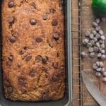 Fresh chocolate chip zucchini bread on a cooling rack next to a chopped zucchini and some scattered chocolate chips.