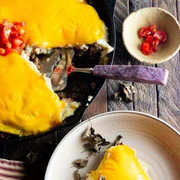 A birds-eye view of cheeseburger pie in a cast iron skillet with a slice up out next to the dish.