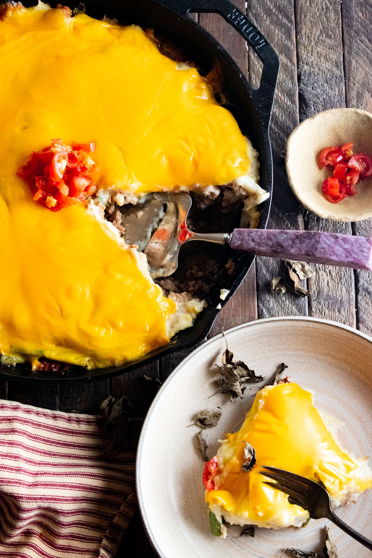 A birds-eye view of cheeseburger pie in a cast-iron skillet with a slice cut out next to the skillet.