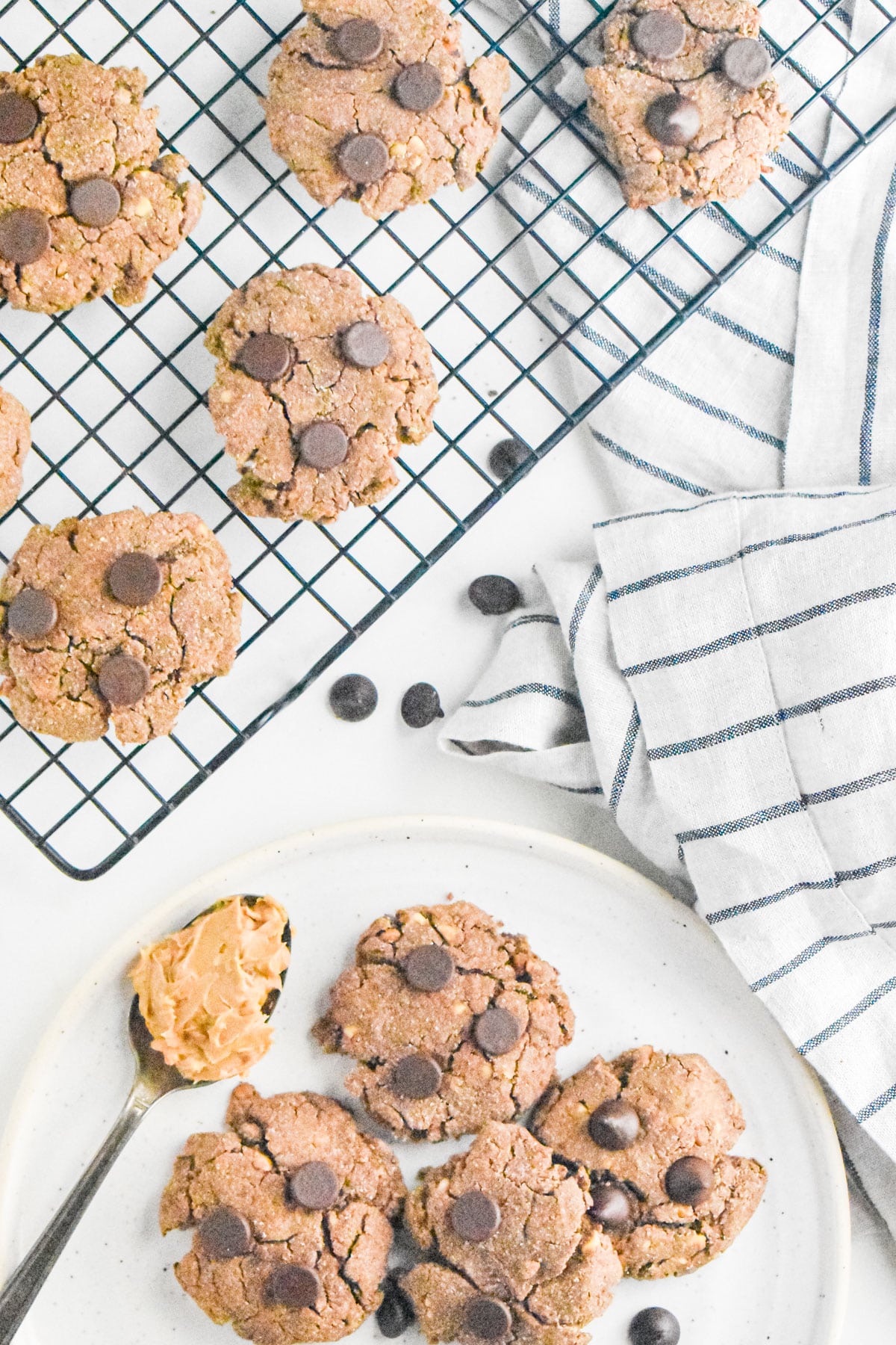 Peanut butter chocolate chip cookies on a cooling rack and a white plate with a stripped colored napkin on the side.