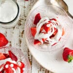 Whipped Cream and strawberries in a clear dish on a white wooden table.
