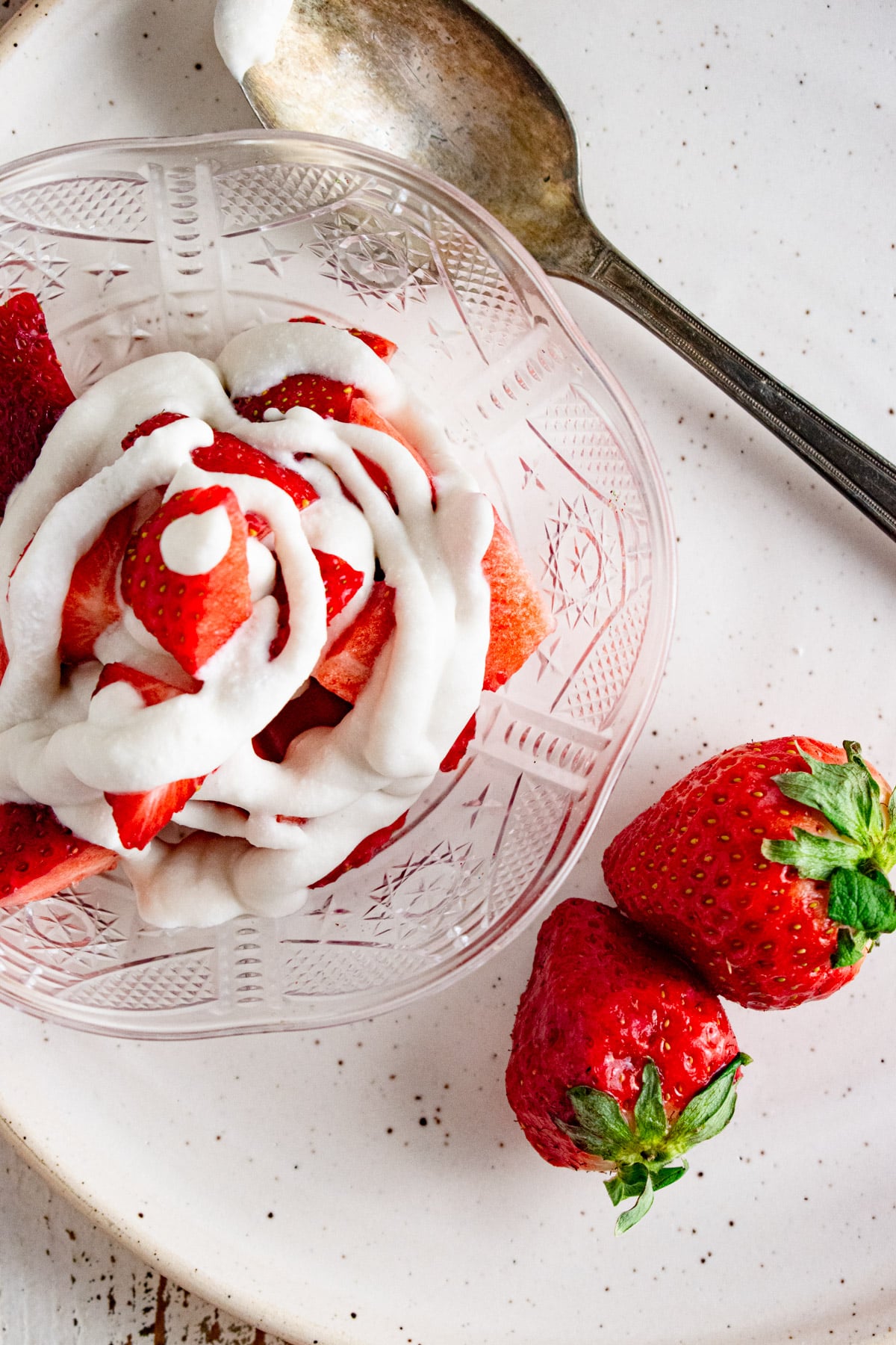 A close up of coconut whipped cream in a clear dish with strawberries laid next to the dish.