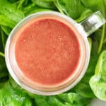 A close up of homemade strawberry vinaigrette dressing on top of a bed of fresh spinach leaves.