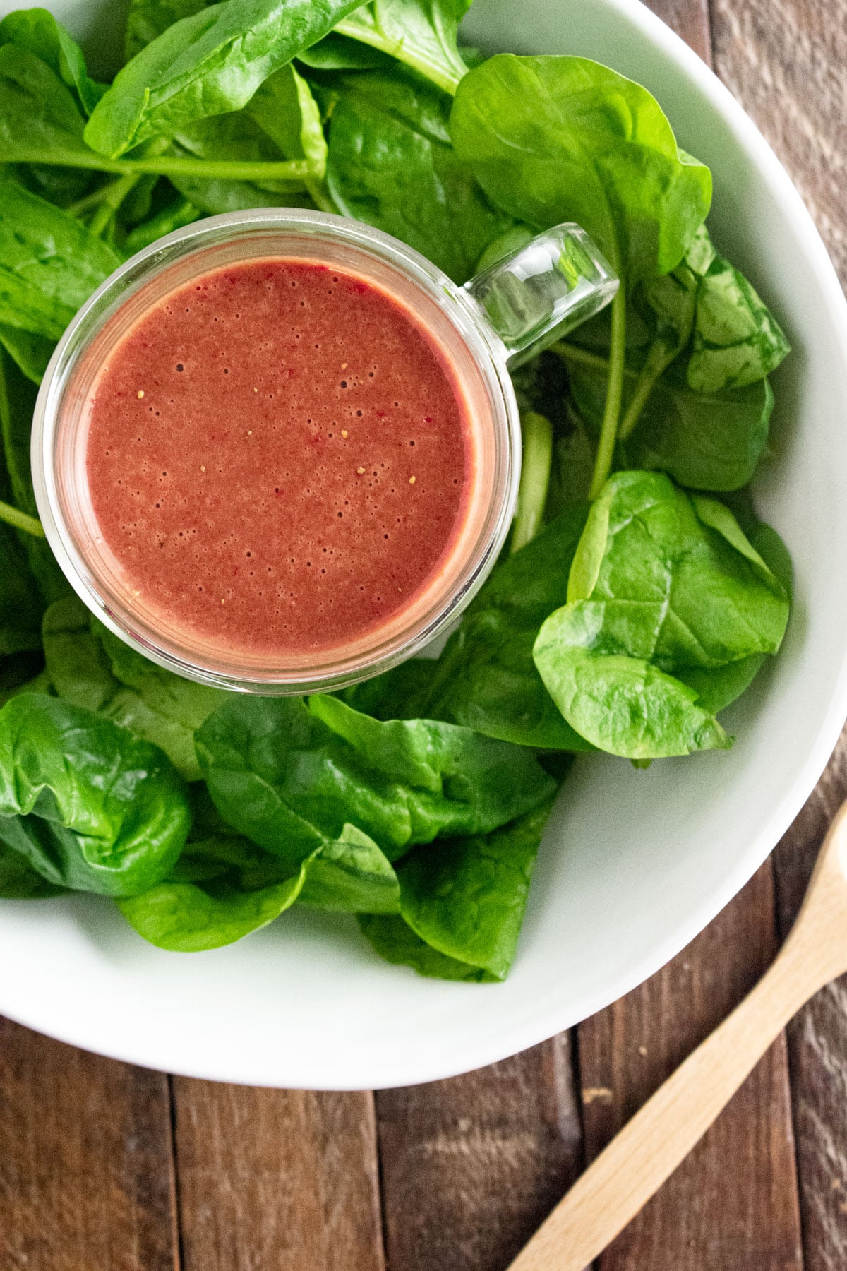 Homemade strawberry dressing in a glass jar sitting on a plate with spinach leaves.
