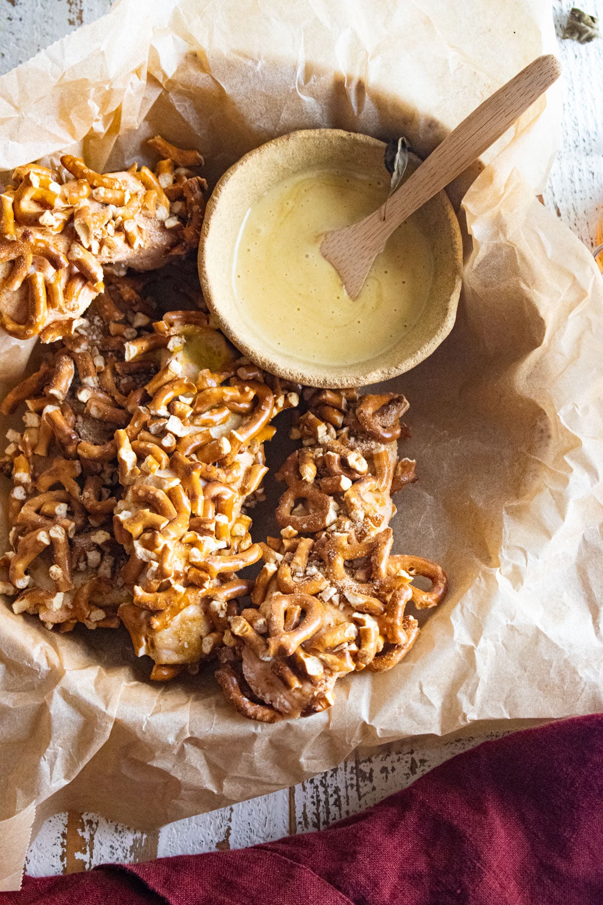 Chicken strips coated in pieces of pretzels in a bowl covered in parchment paper and a side of honey mustard.
